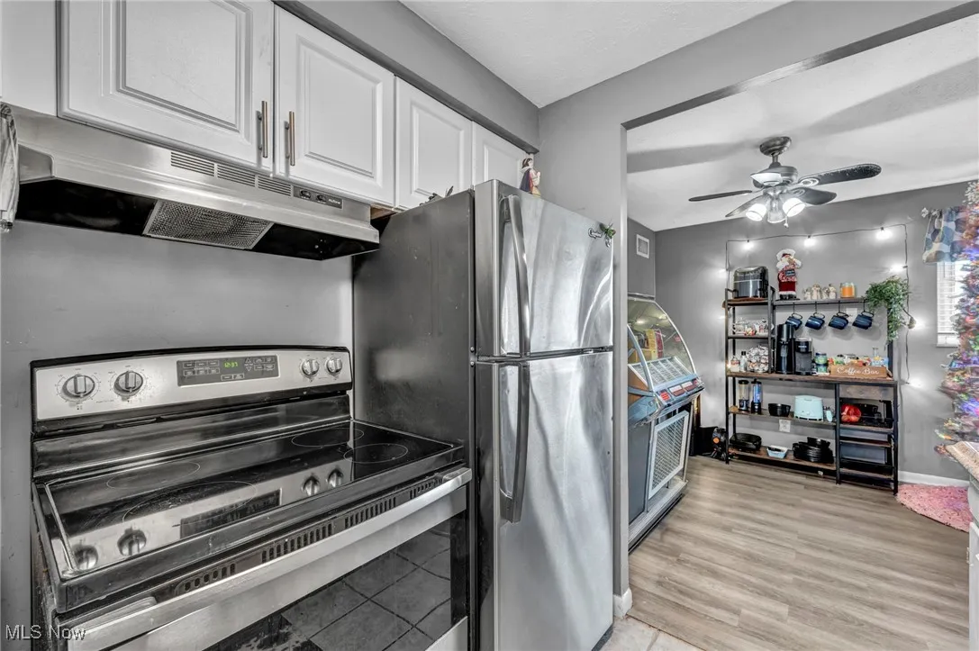 Kitchen with stainless steel electric stove, under cabinet range hood, white cabinets, a ceiling fan, and light wood finished floors