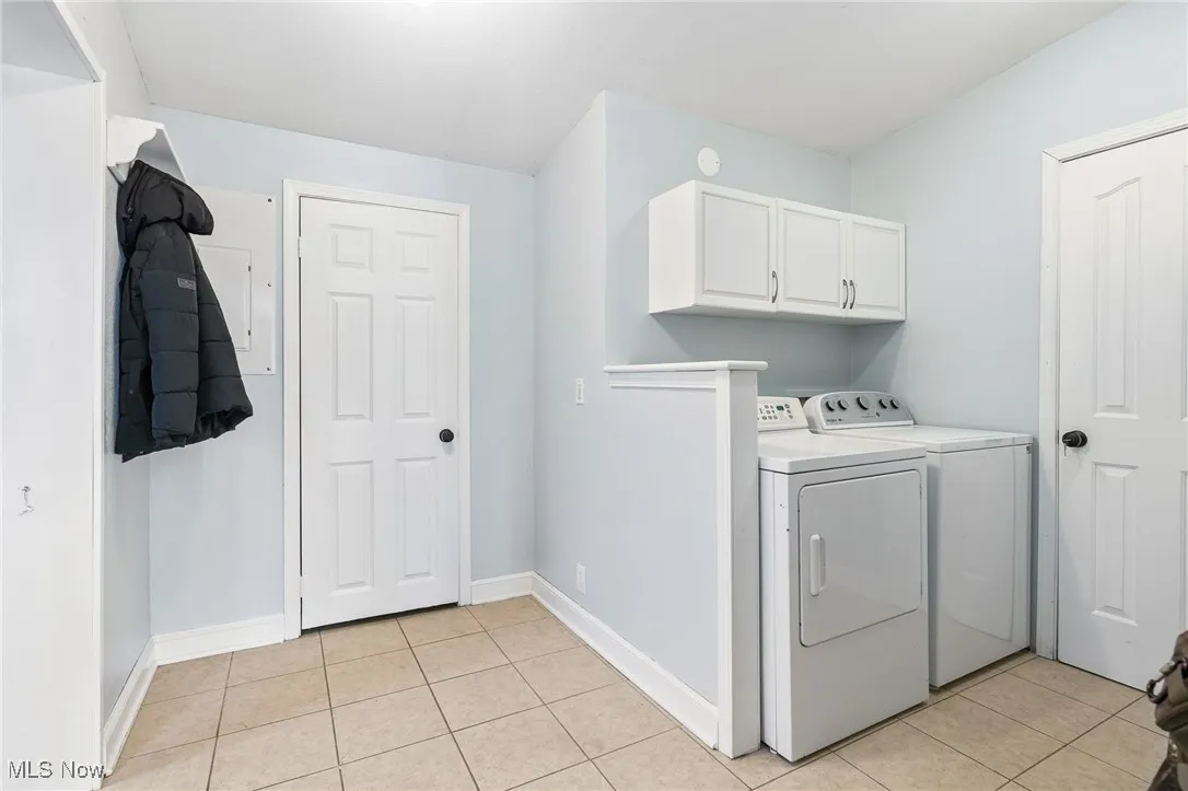 Laundry area featuring light tile patterned floors, independent washer and dryer, and cabinet space