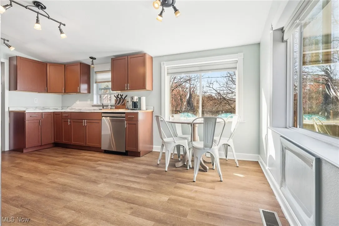 Kitchen with brown cabinets, light countertops, light wood-style floors, stainless steel dishwasher, and rail lighting