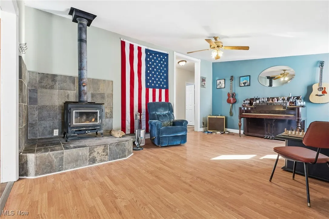 Living room with a wood stove, wood finished floors, and a ceiling fan