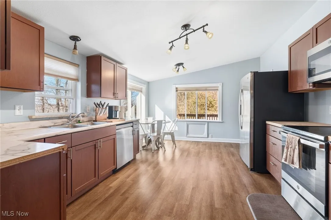 Kitchen with stainless steel appliances, brown cabinets, light wood-style floors, light countertops, and lofted ceiling