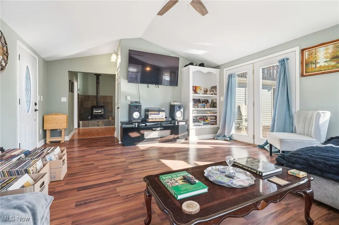 Living area with wood finished floors, lofted ceiling, a wood stove, and ceiling fan