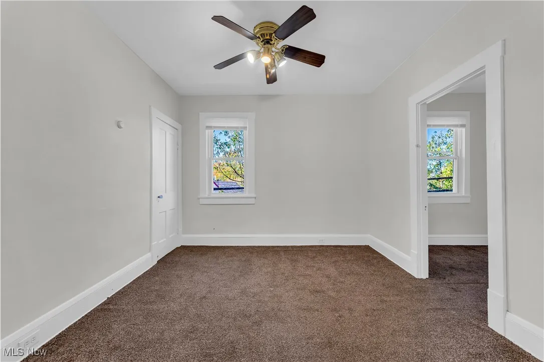 Unfurnished room featuring dark colored carpet and ceiling fan
