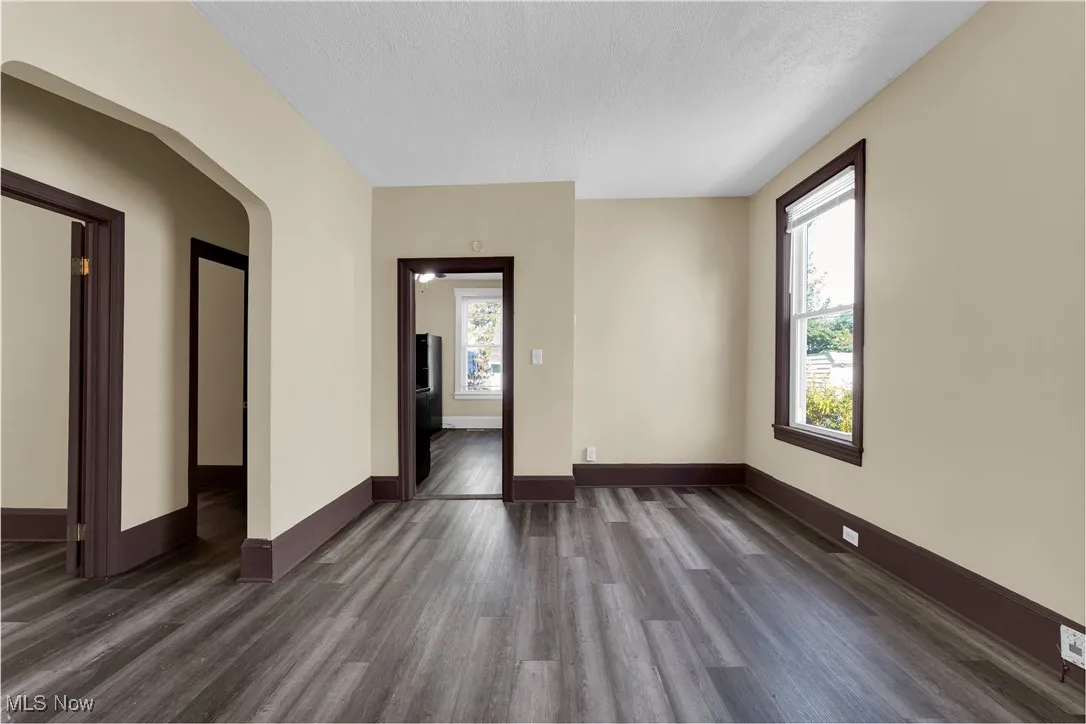 Empty room with dark wood finished floors, plenty of natural light, arched walkways, and a textured ceiling
