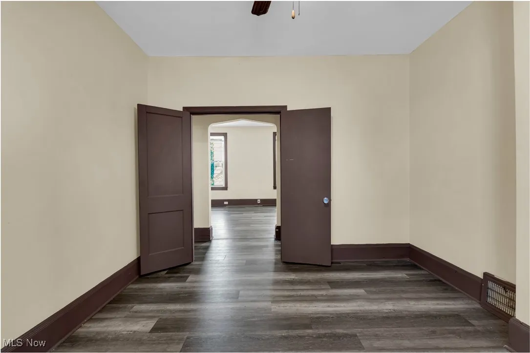 Empty room with dark wood-type flooring, arched walkways, and a ceiling fan