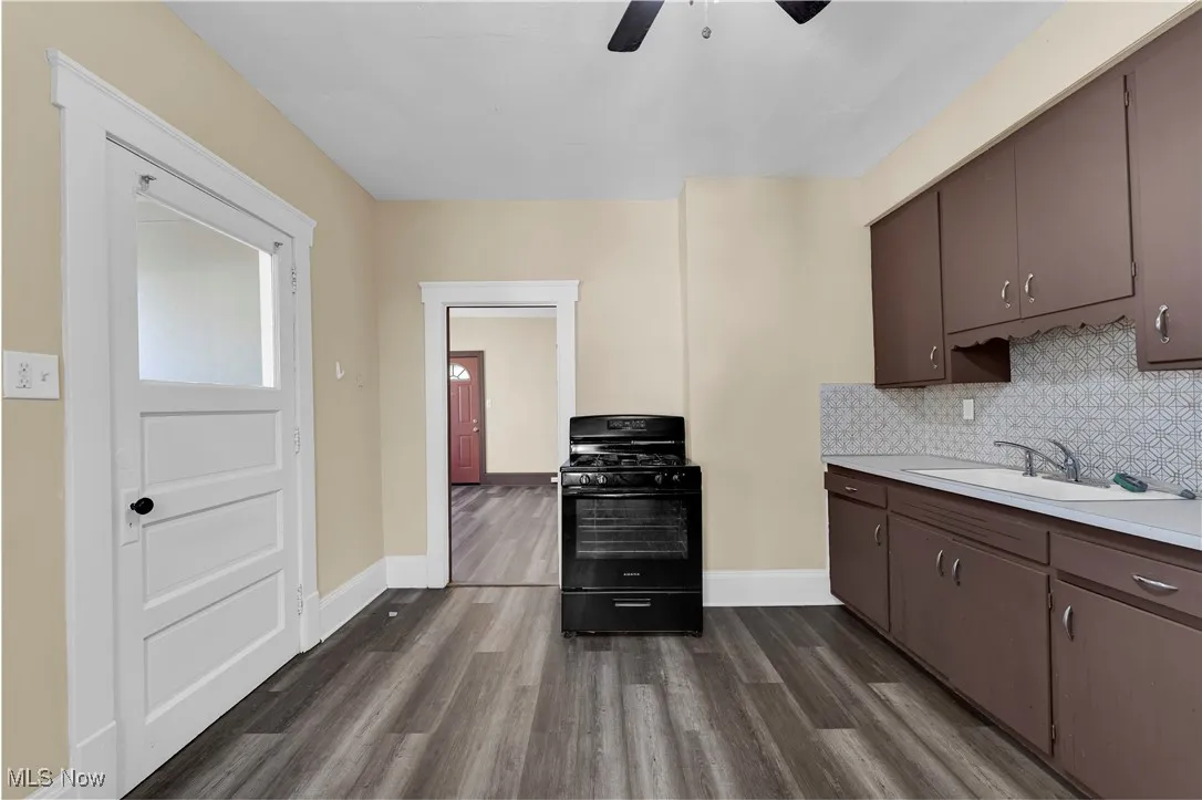 Kitchen featuring black range with gas cooktop, light countertops, dark wood-type flooring, tasteful backsplash, and dark brown cabinetry