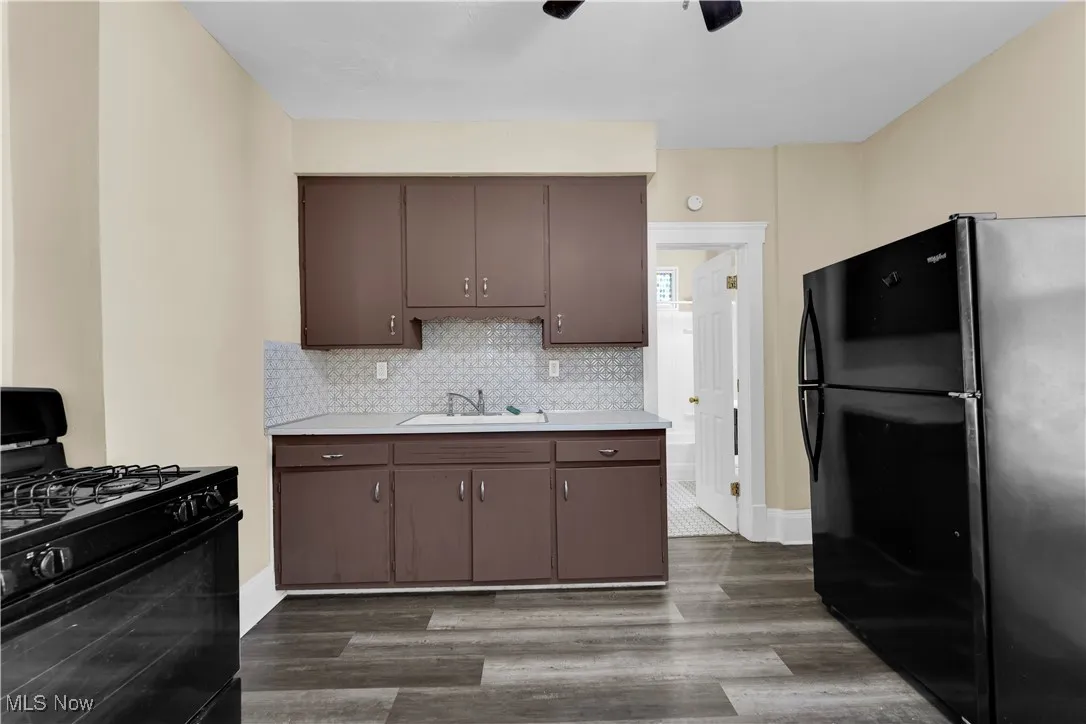 Kitchen featuring black appliances, light countertops, dark wood-style floors, backsplash, and dark brown cabinets