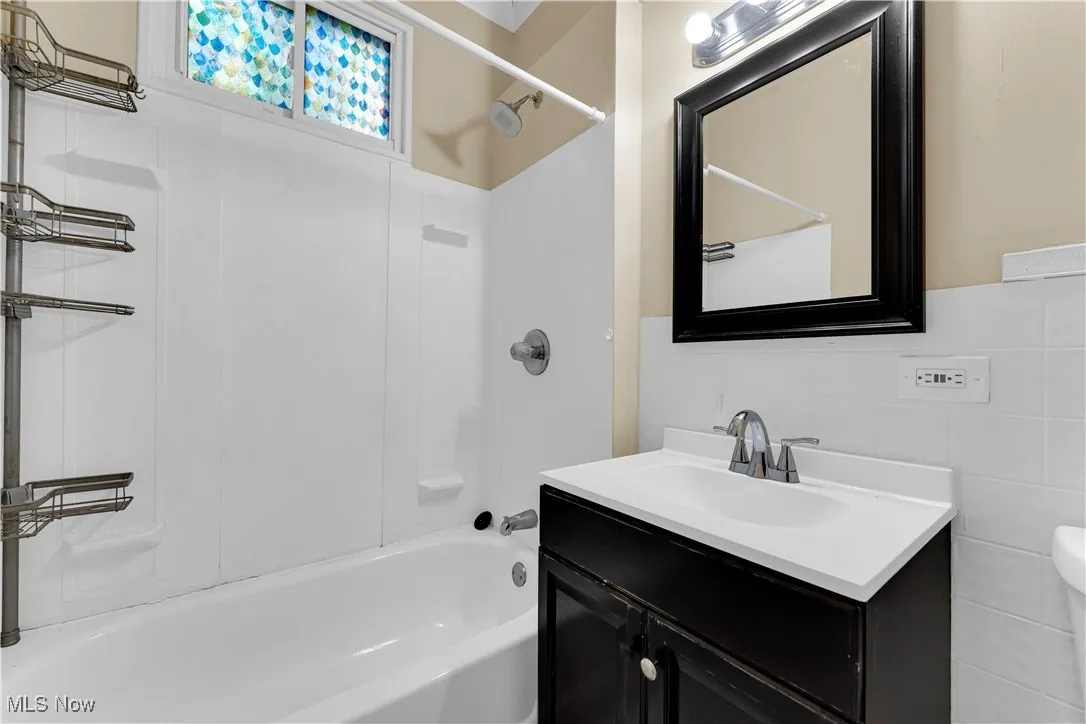 Bathroom with shower / washtub combination, vanity, and tile walls