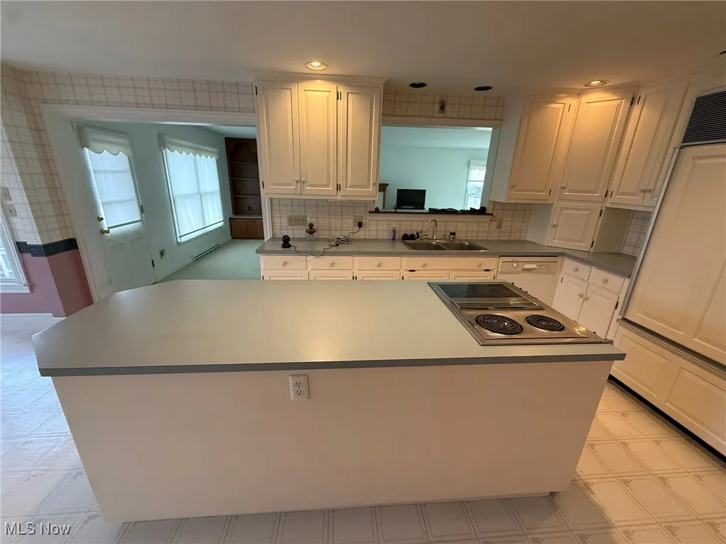 Kitchen featuring a kitchen island, light floors, decorative backsplash, stainless steel electric cooktop, and white cabinetry