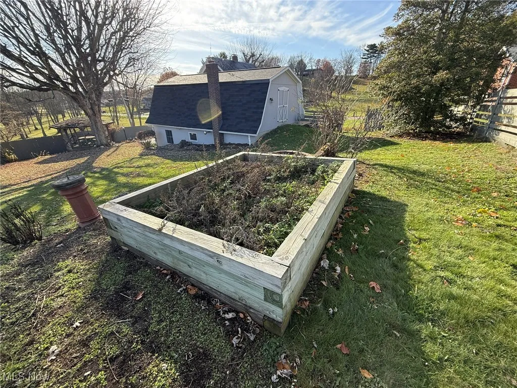 Back of property featuring a vegetable garden, a gambrel roof, a chimney, a shed, and a shingled roof