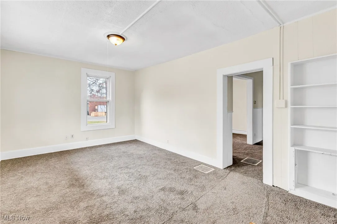 Unfurnished room featuring built in shelves, light colored carpet, and a textured ceiling