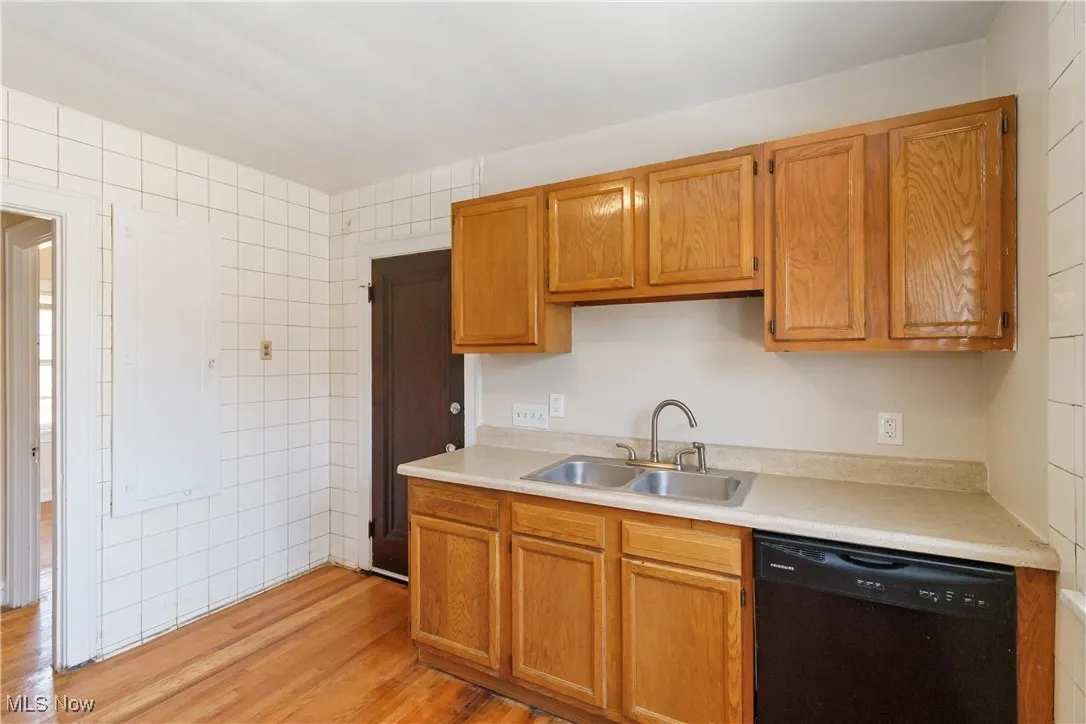1st Floor Kitchen featuring black dishwasher, light wood-style floors, light countertops, tile walls, and brown cabinetry