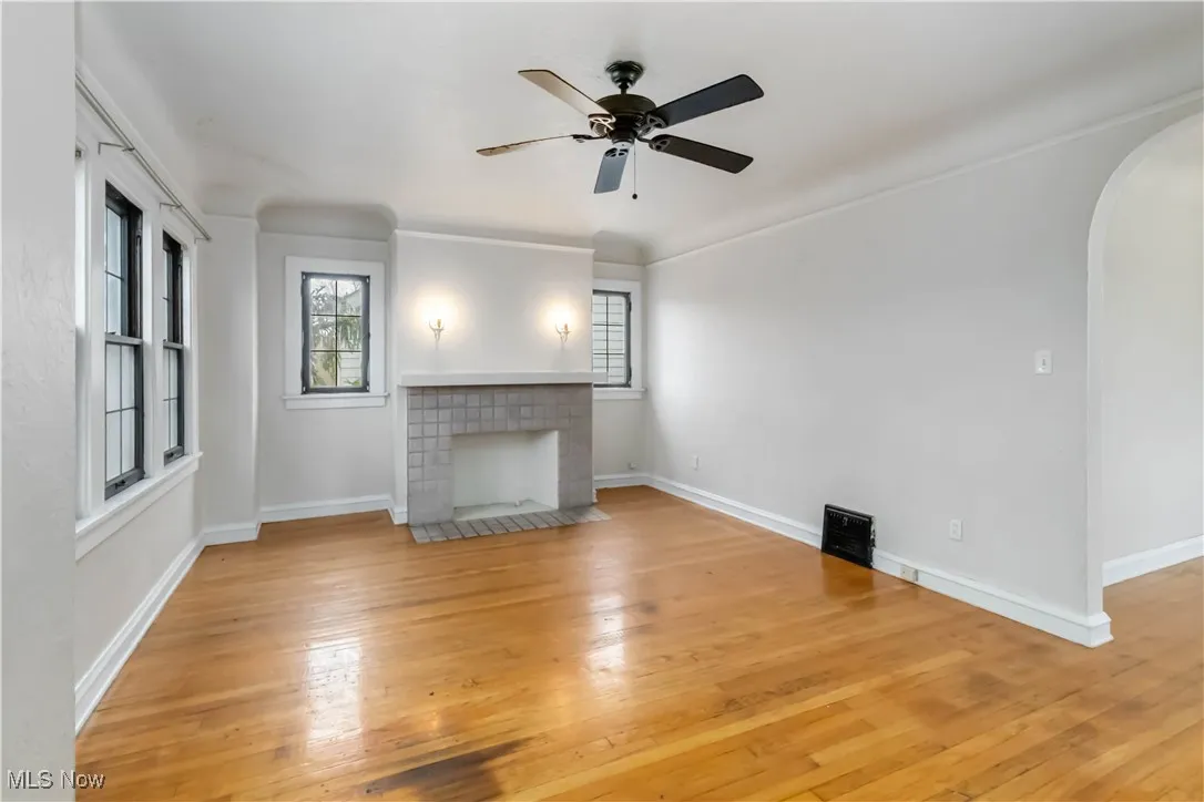 2nd floor living room featuring arched walkways, a ceiling fan, light wood finished floors, and a fireplace with flush hearth
