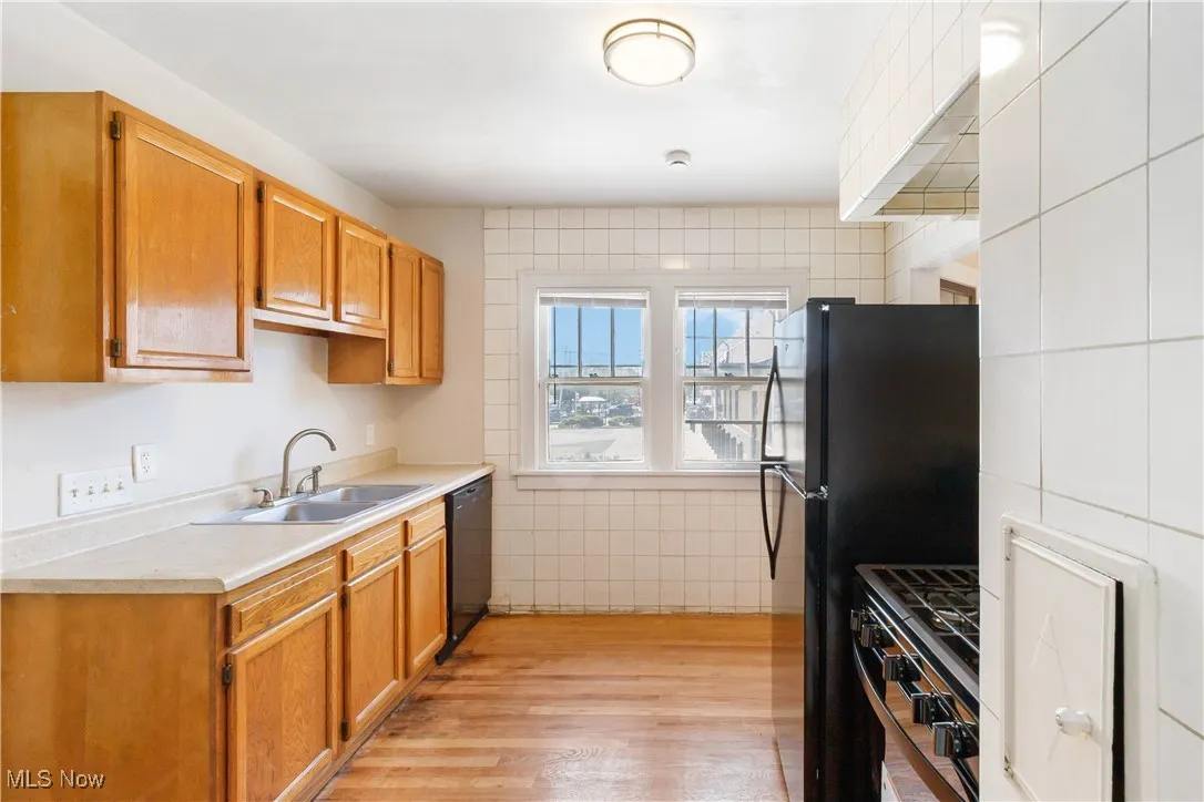 1st Floor Kitchen with light wood-style flooring, black appliances, light countertops, tile walls, and brown cabinets