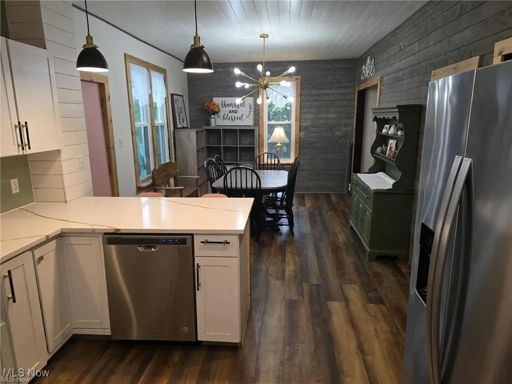 Kitchen with appliances with stainless steel finishes, white cabinets, wood walls, and pendant lighting