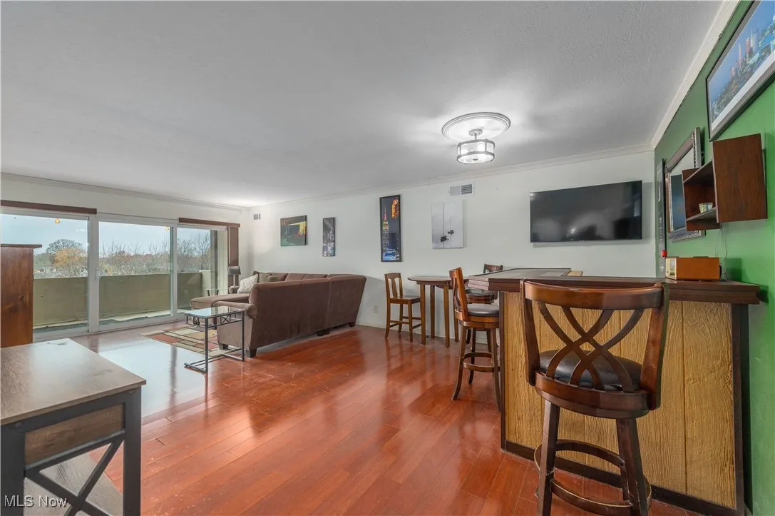 Living area featuring ornamental molding, wood finished floors, and a bar