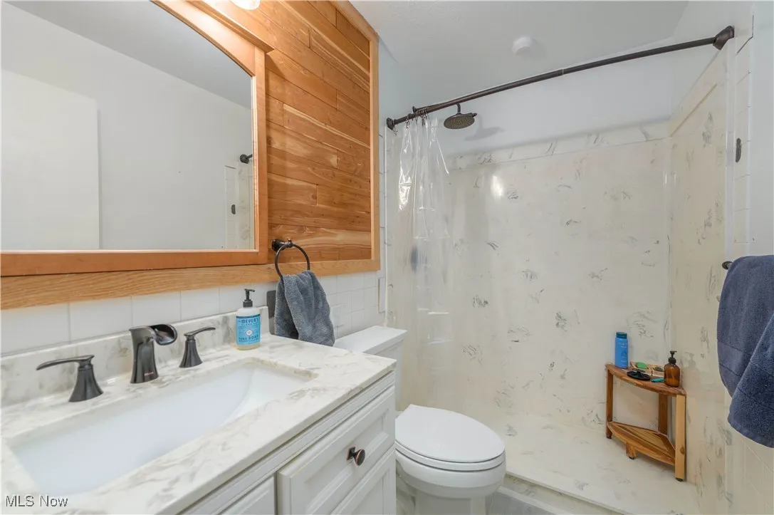 Full bath featuring a shower stall, vanity, tasteful backsplash, and tile walls