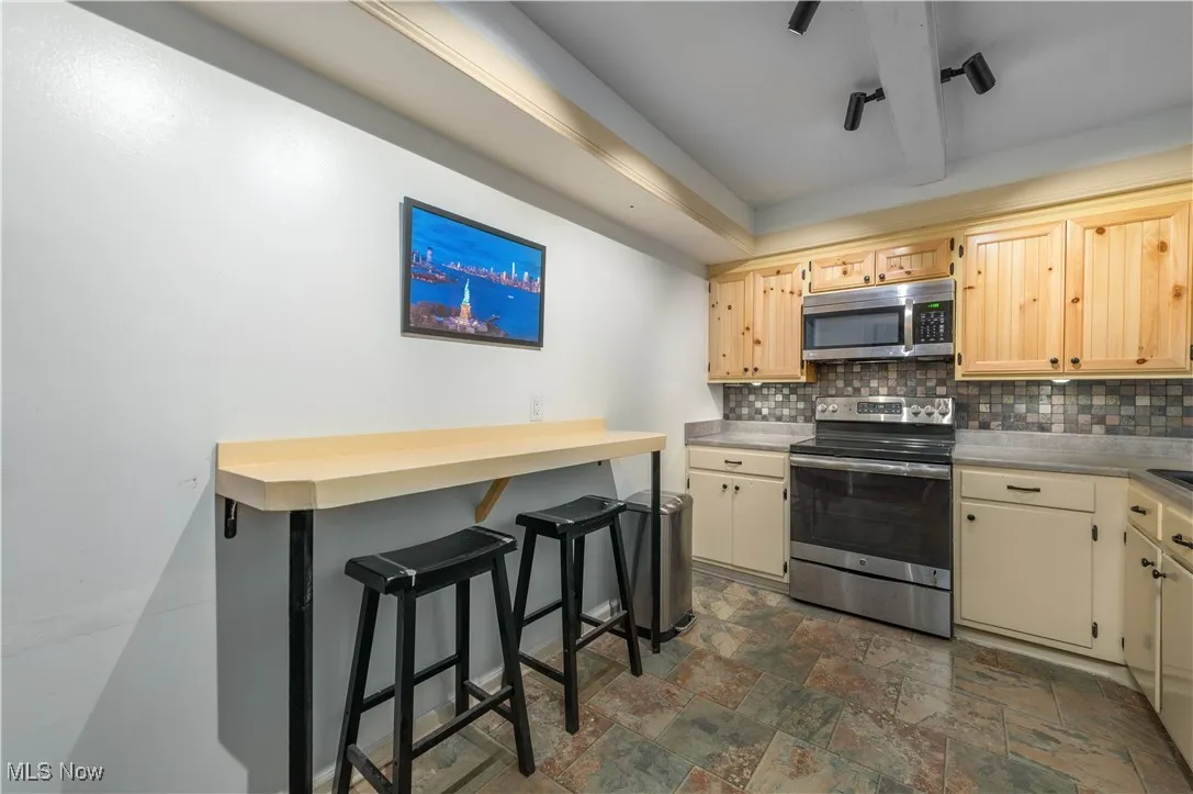 Kitchen featuring stainless steel appliances, a breakfast bar area, backsplash, light countertops, and dark stone finish flooring