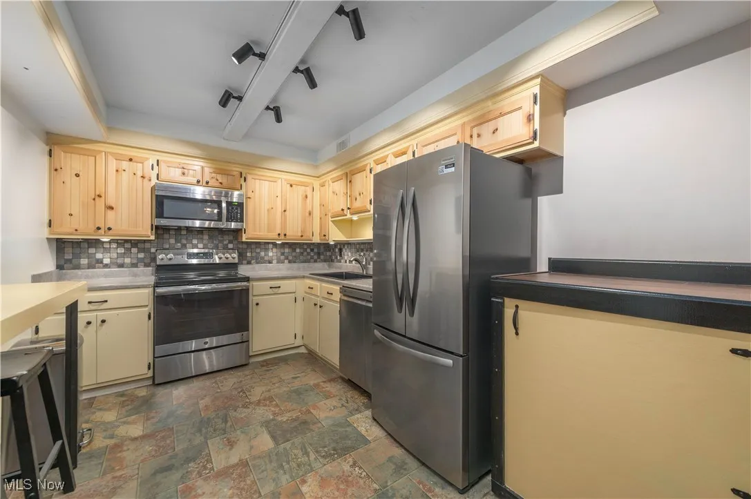 Kitchen with appliances with stainless steel finishes, tasteful backsplash, a tray ceiling, light countertops, and dark stone finish flooring