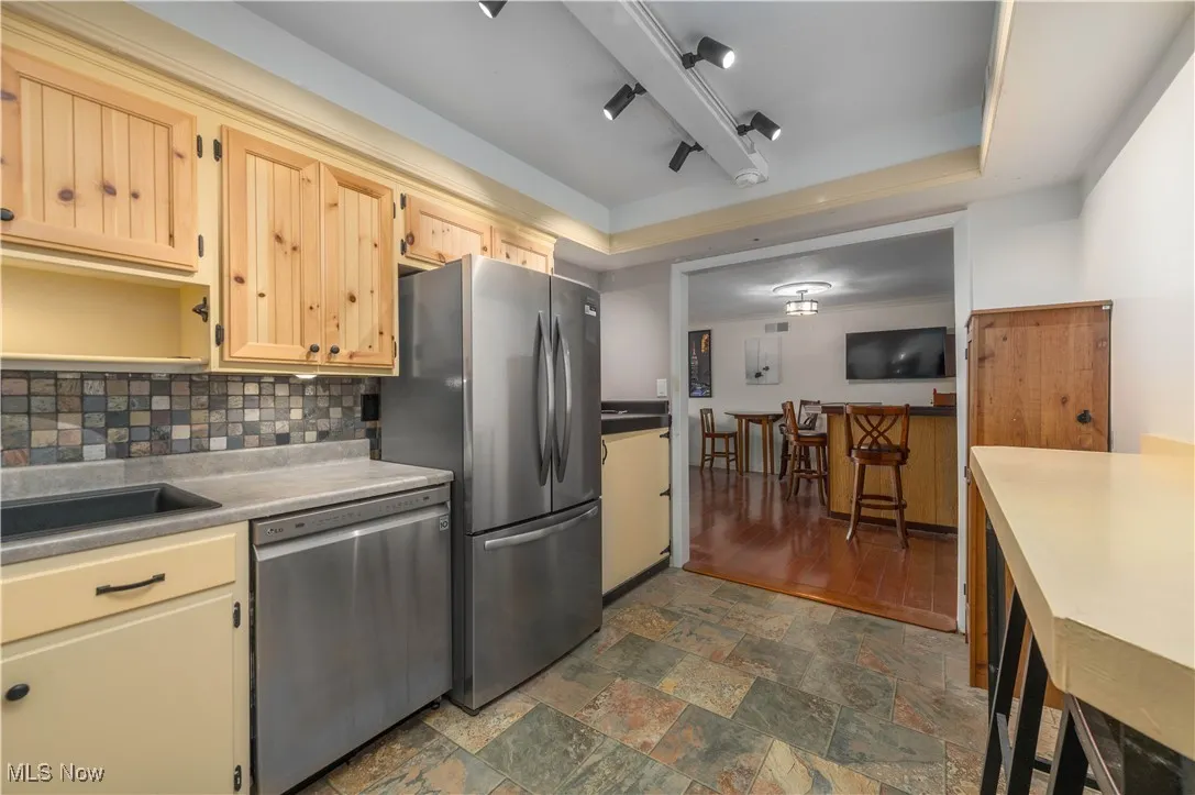 Kitchen featuring stainless steel appliances, a raised ceiling, backsplash, light countertops, and dark stone finish floors