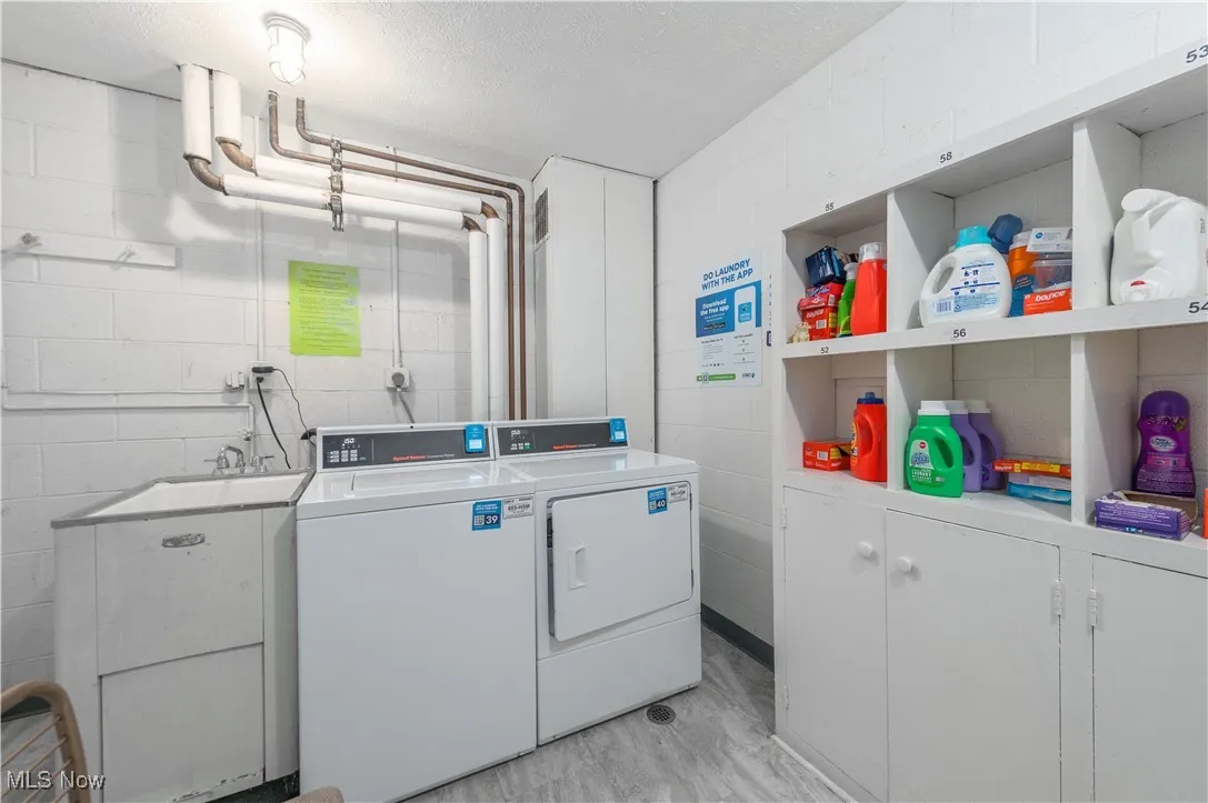 Community laundry with washing machine and dryer, a textured ceiling, concrete block wall, and light wood-type flooring