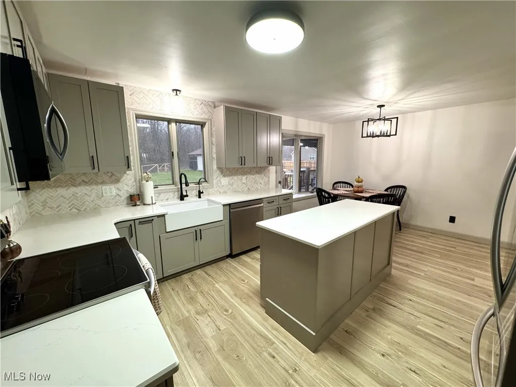 Kitchen featuring gray cabinetry, a kitchen island, decorative light fixtures, backsplash, and range with electric cooktop