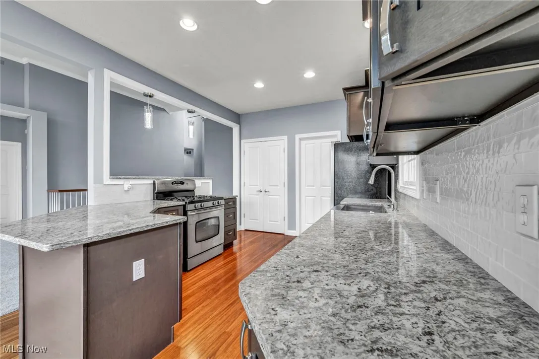 Kitchen with gas stove, light stone countertops, light wood-style floors, hanging light fixtures, and recessed lighting