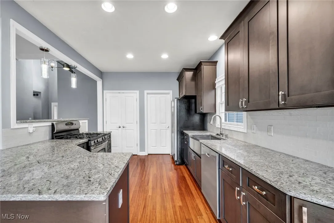 Kitchen featuring dark brown cabinets, tasteful backsplash, light wood-type flooring, light stone countertops, and stainless steel appliances
