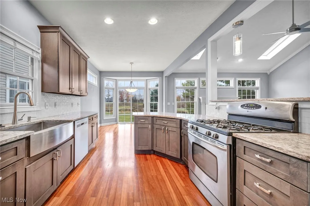 Kitchen featuring decorative backsplash, decorative light fixtures, stainless steel range with gas cooktop, light wood-style flooring, and light stone counters