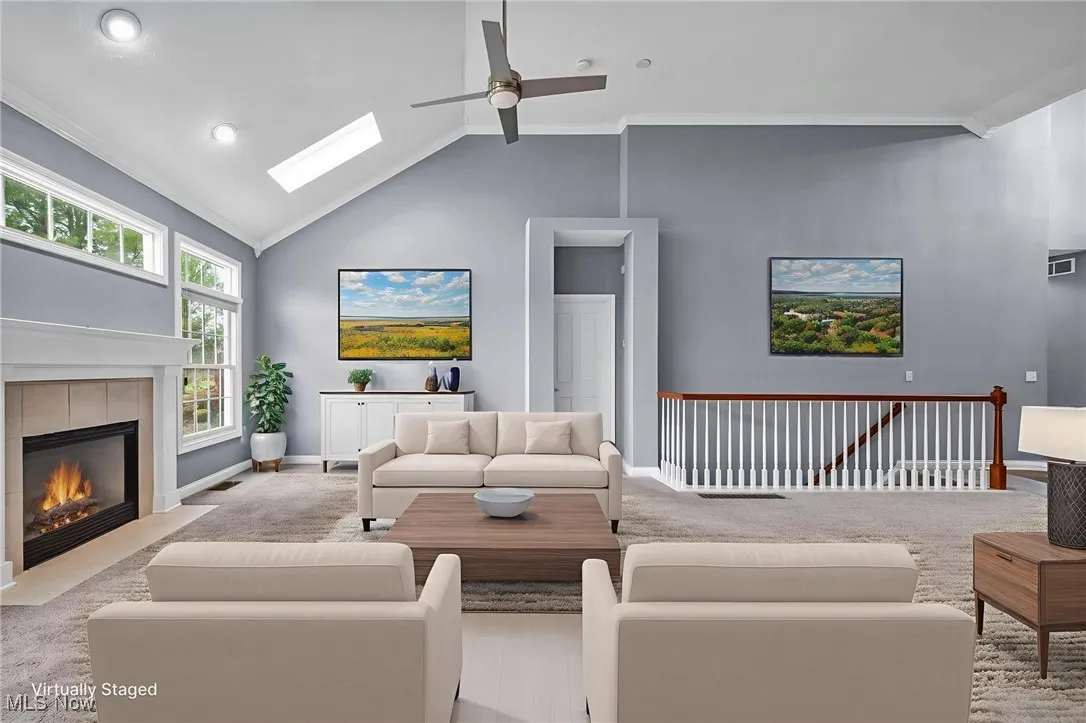 Carpeted living area featuring crown molding, lofted ceiling, a skylight, ceiling fan, and a tile fireplace