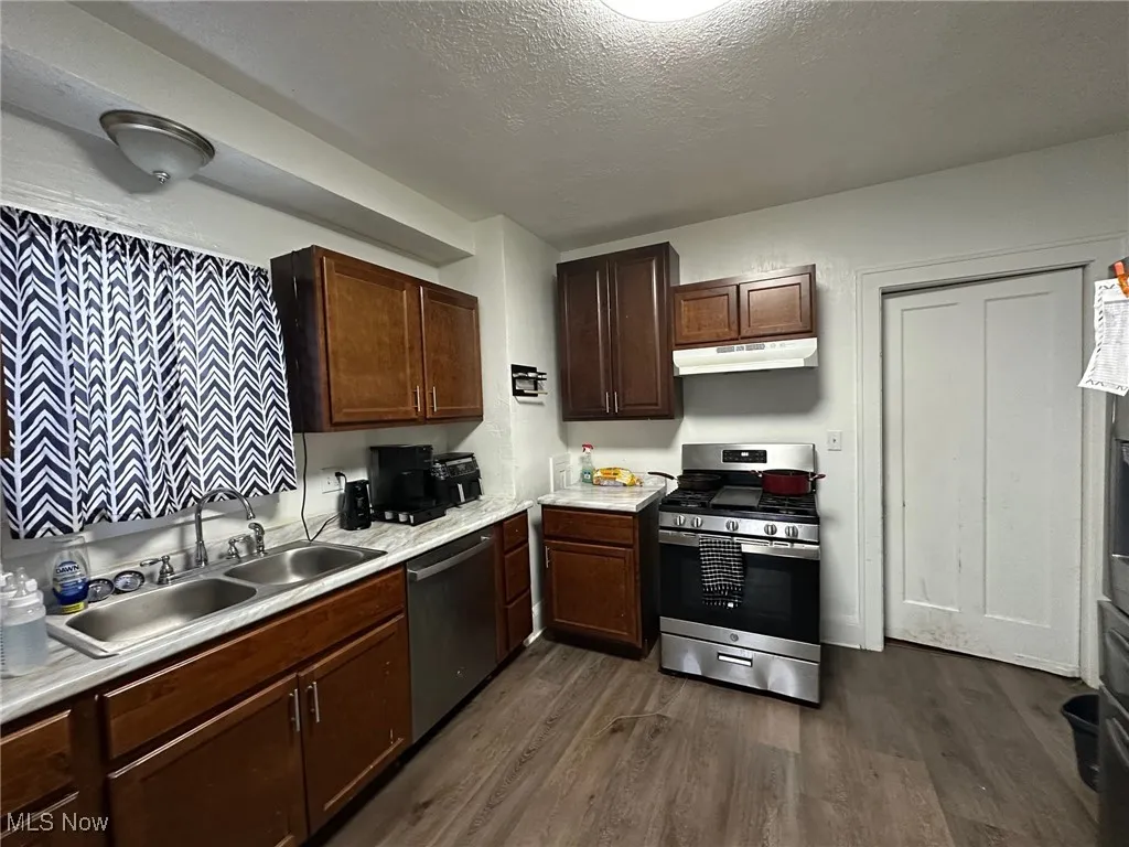 Kitchen featuring appliances with stainless steel finishes, light countertops, dark wood-style floors, dark brown cabinets, and a textured ceiling