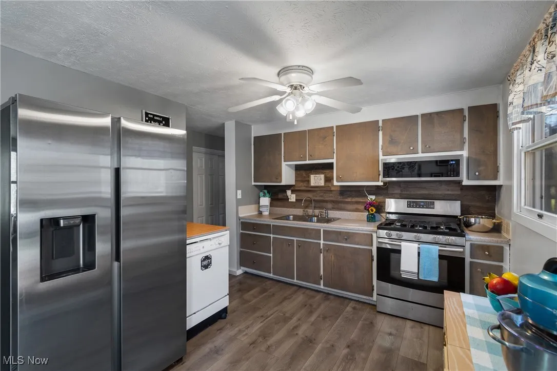 Kitchen with stainless steel appliances, light countertops, wood laminate flooring, ceiling fan, and a textured ceiling