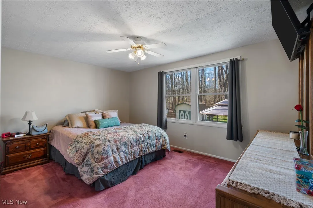 Bedroom with carpet flooring, a ceiling fan, double windows and a textured ceiling