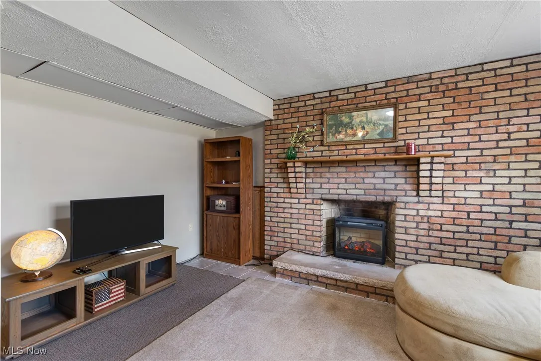 Lower level living area with carpet and tile, wood paneling, a textured ceiling, brick fireplace with electric insert and two windows