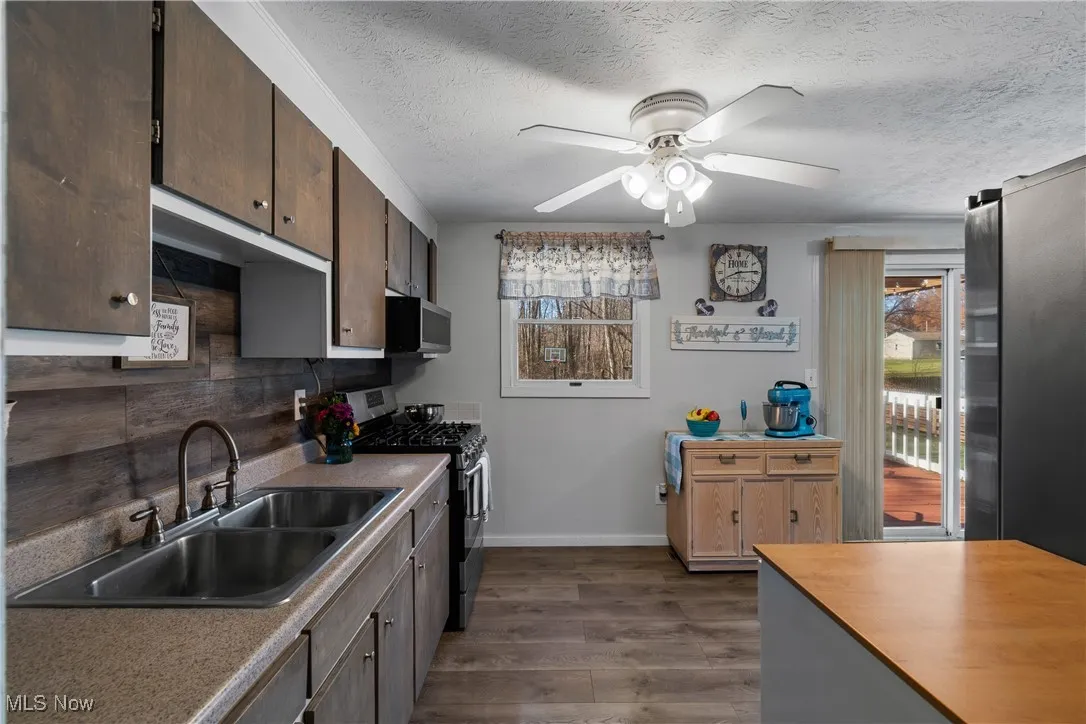 Kitchen with stainless steel appliances, wood laminate flooring, decorative backsplash, a textured ceiling, window and a ceiling fan