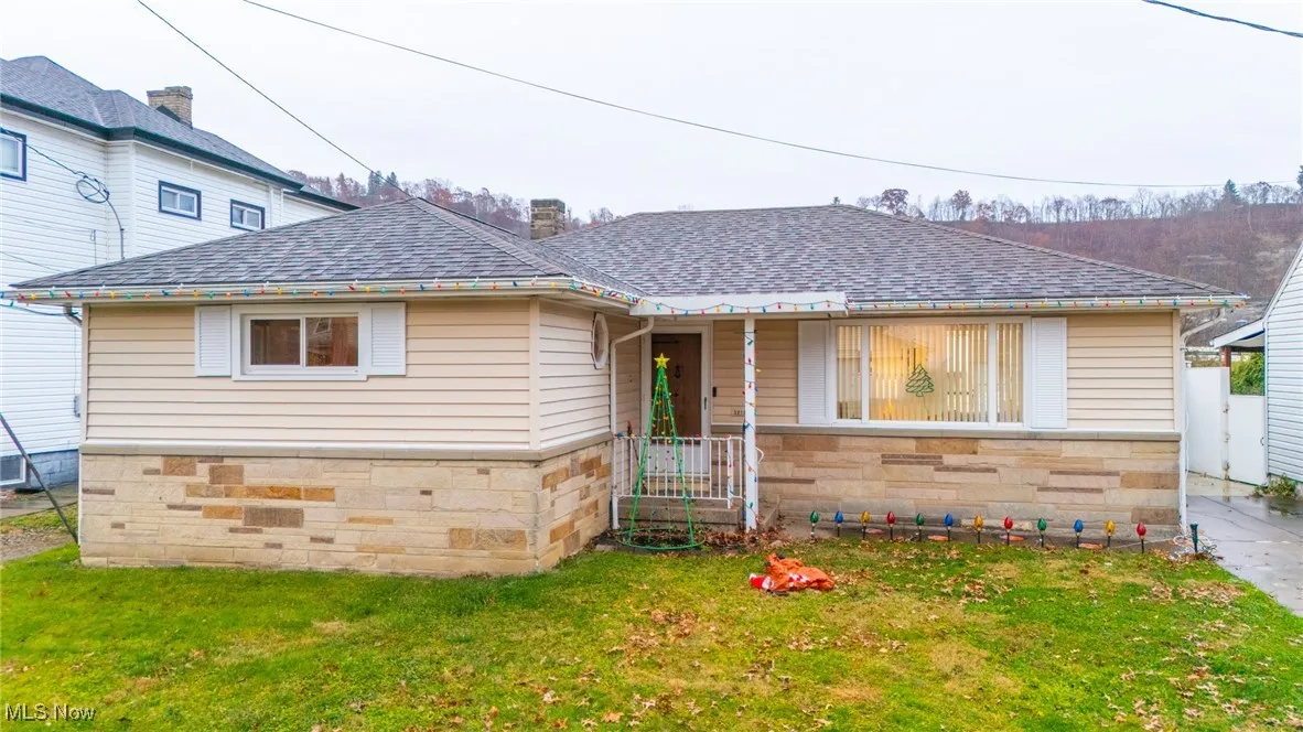 View of front of home featuring roof with shingles, a front yard, and stone siding
