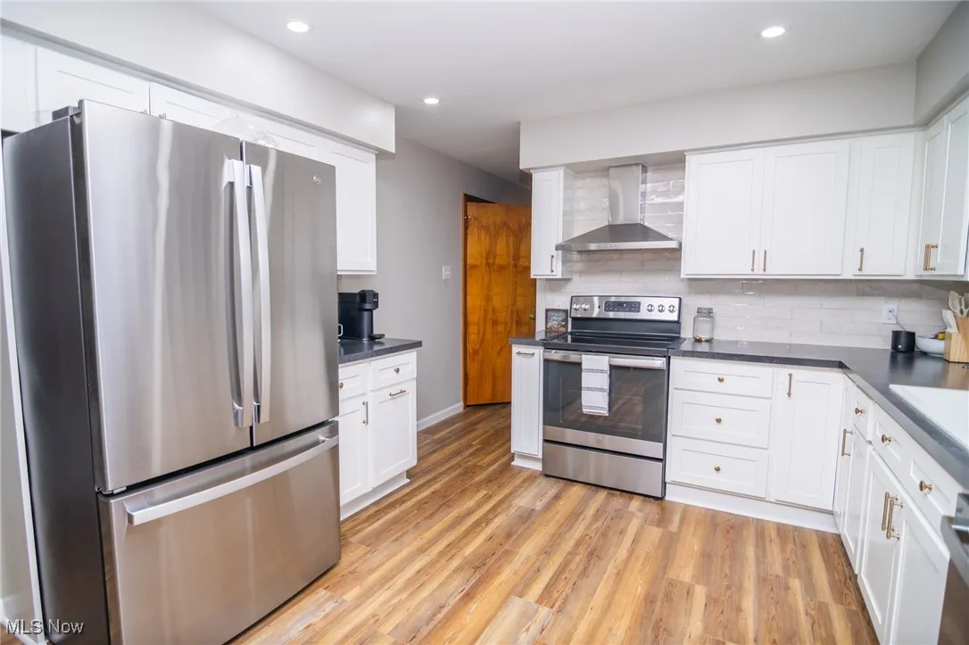 Kitchen with appliances with stainless steel finishes, wall chimney exhaust hood, light wood-type flooring, white cabinets, and recessed lighting