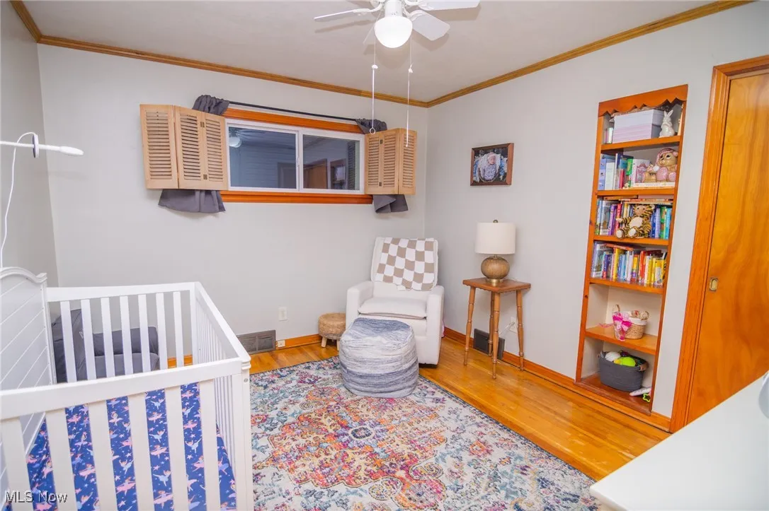 Bedroom with ornamental molding, a nursery area, wood finished floors, and a ceiling fan