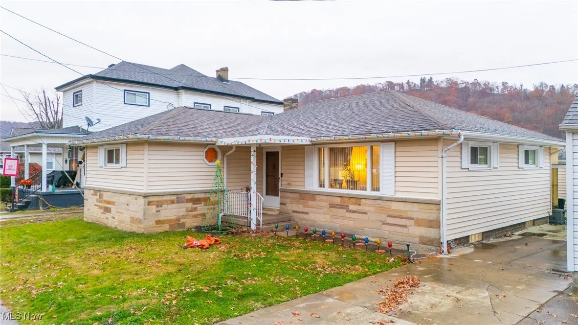 View of front of home featuring a front yard, stone siding, and a shingled roof