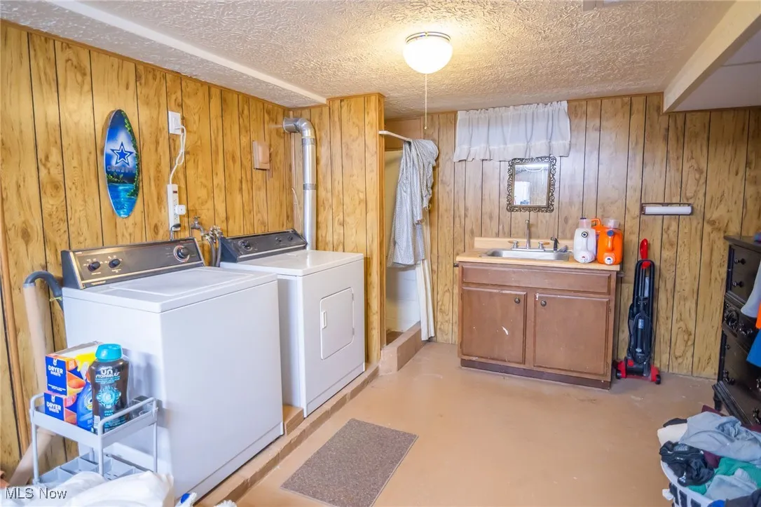 Laundry room featuring wood walls, washing machine and dryer, finished concrete floors, and a textured ceiling