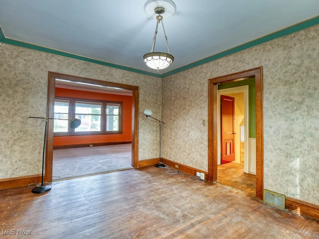 Unfurnished room featuring wallpapered walls, wood finished floors, and crown molding