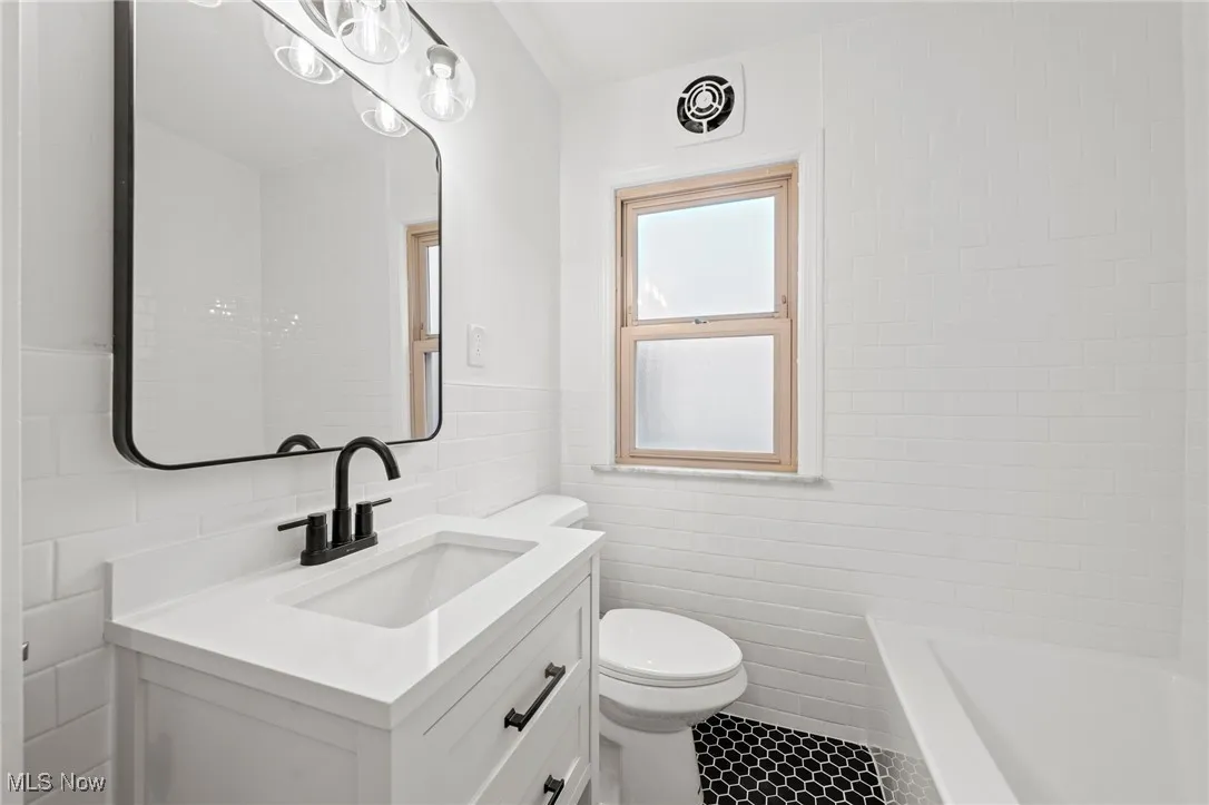 Full bath with tile walls, vanity, a tub to relax in, and tile patterned flooring