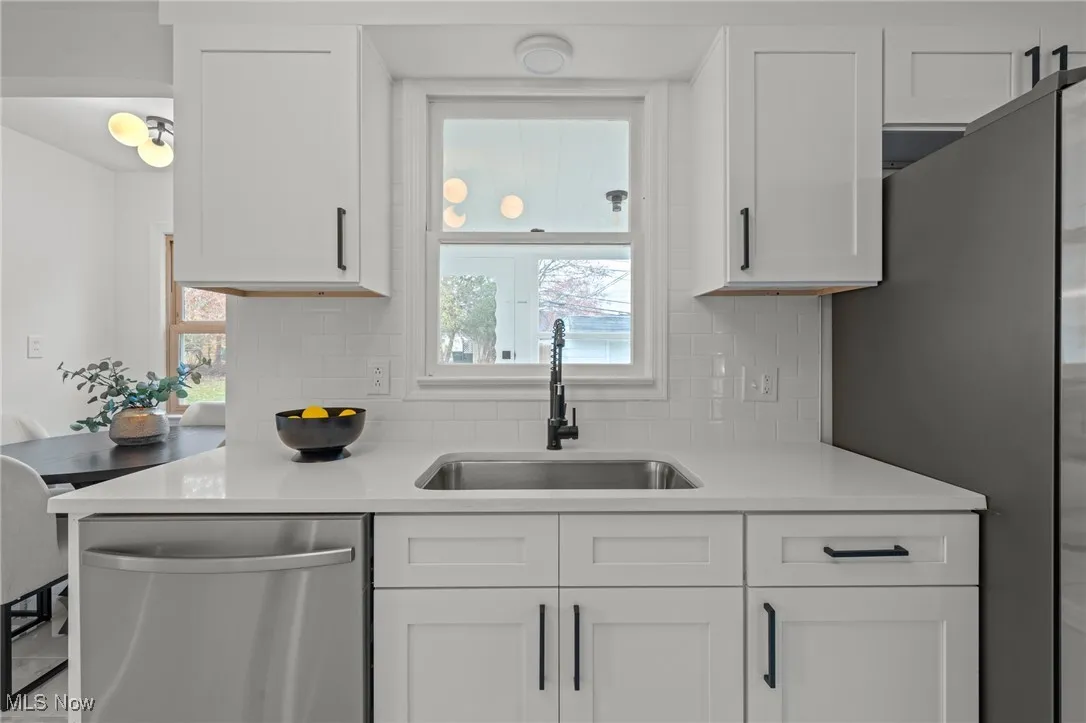 Kitchen with stainless steel appliances, white cabinetry, decorative backsplash, and light stone countertops