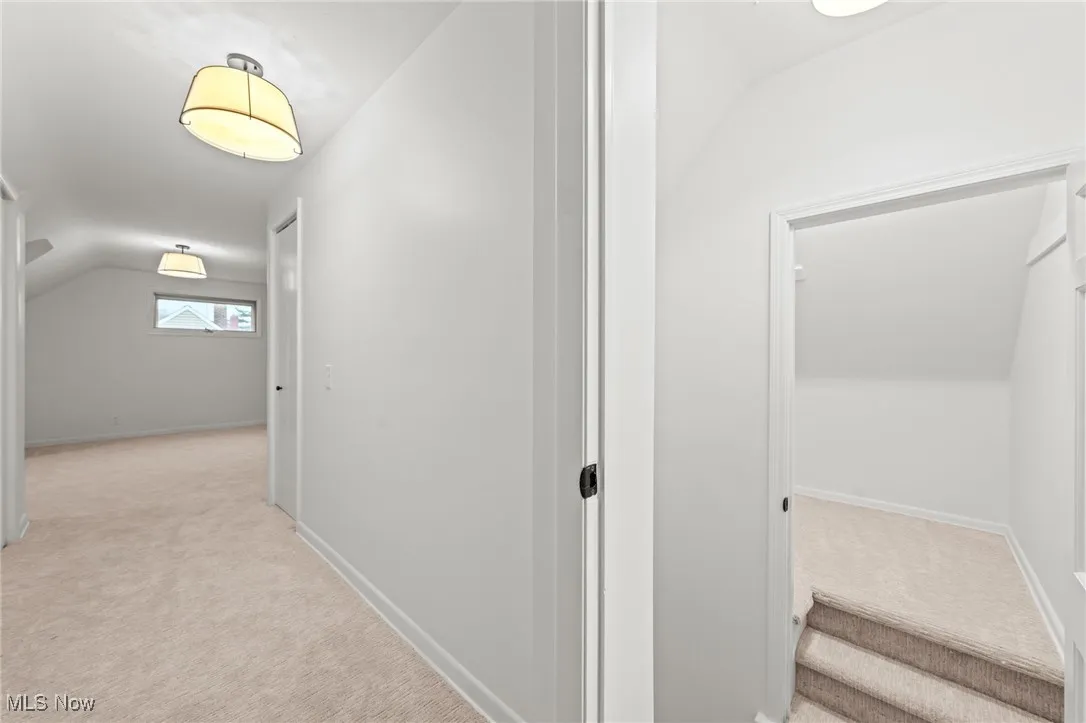 Hallway with light colored carpet and lofted ceiling