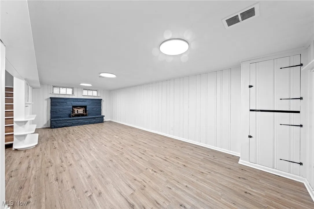 Unfurnished living room with light wood-type flooring, a stone fireplace, and wood walls