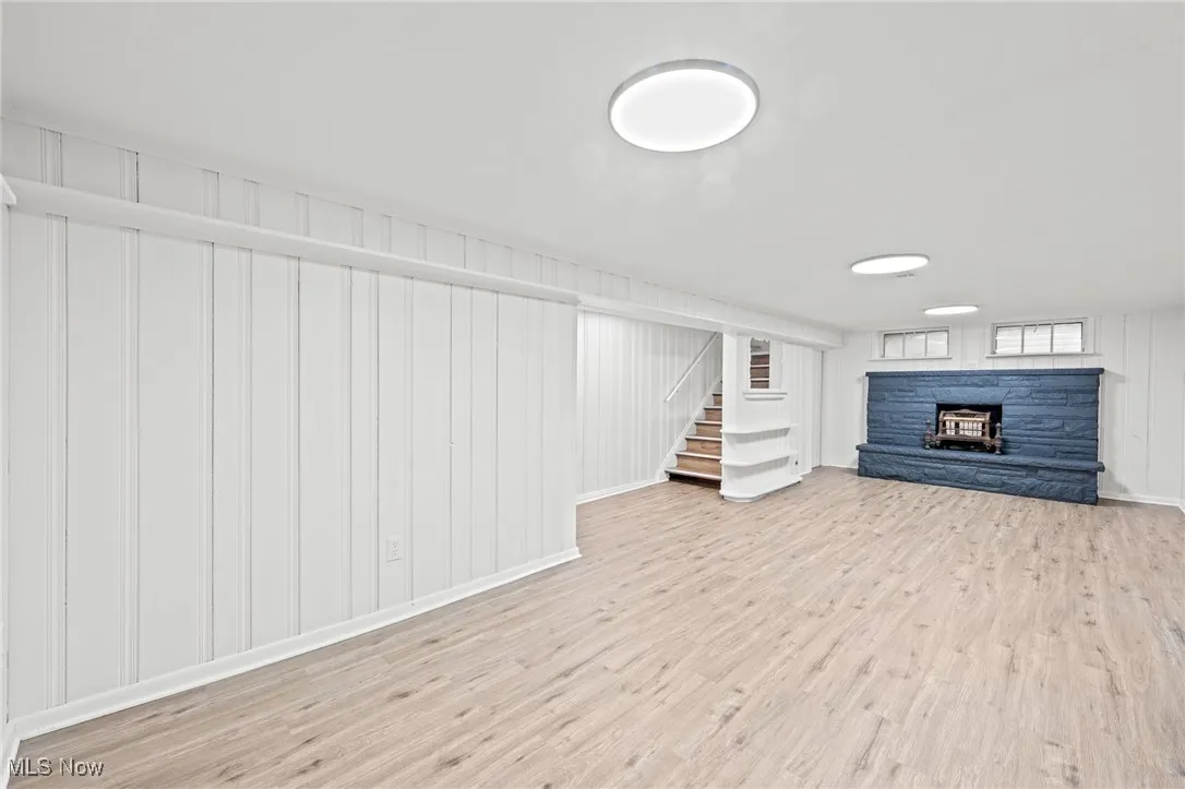 Basement featuring light wood finished floors, a fireplace, stairs, and wooden walls