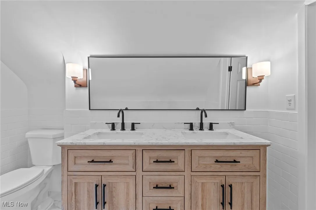 Bathroom featuring tile walls, a wainscoted wall, and double vanity