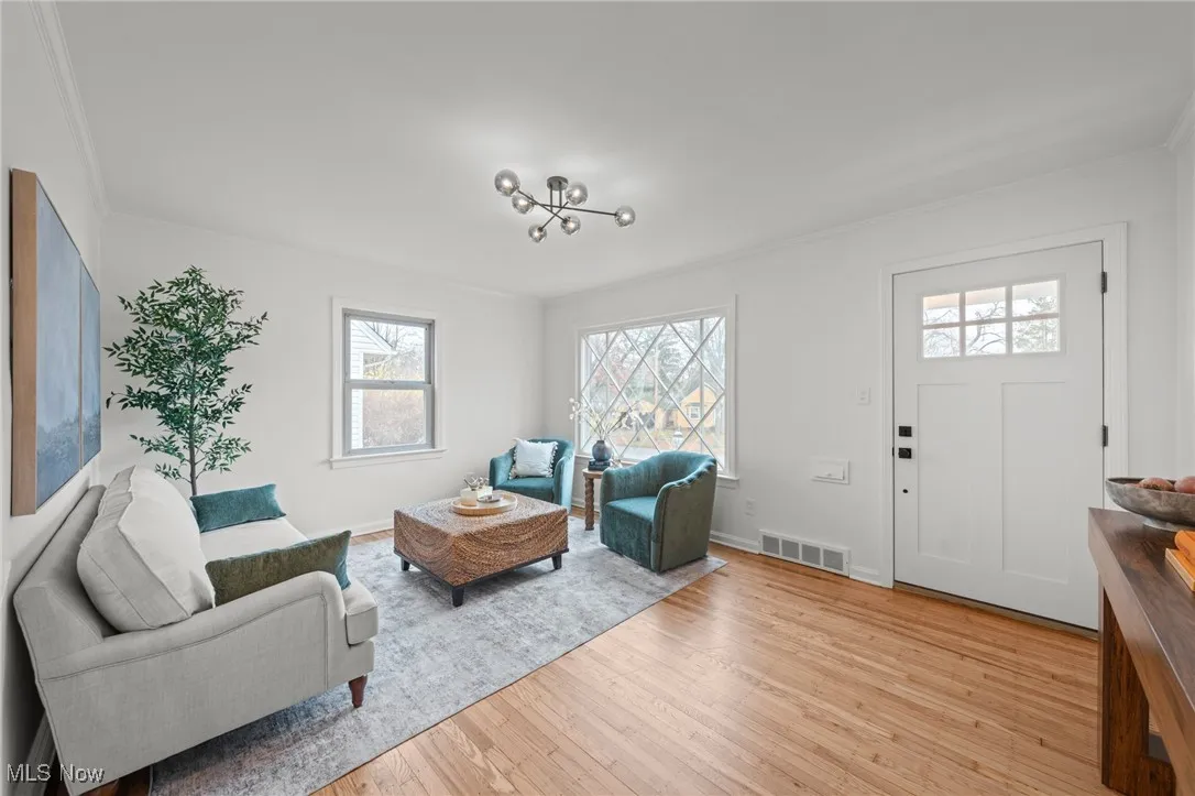 Living area featuring crown molding, light wood-style flooring, and a chandelier