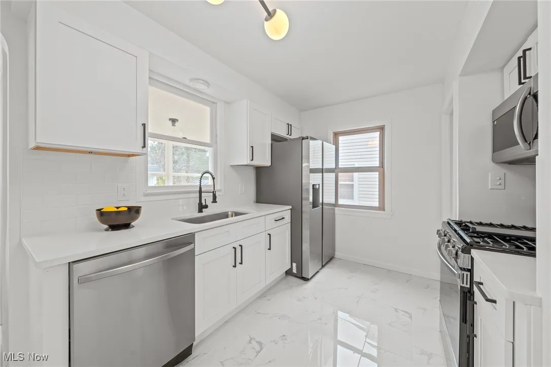 Kitchen with stainless steel appliances, light marble finish flooring, white cabinets, and light stone countertops