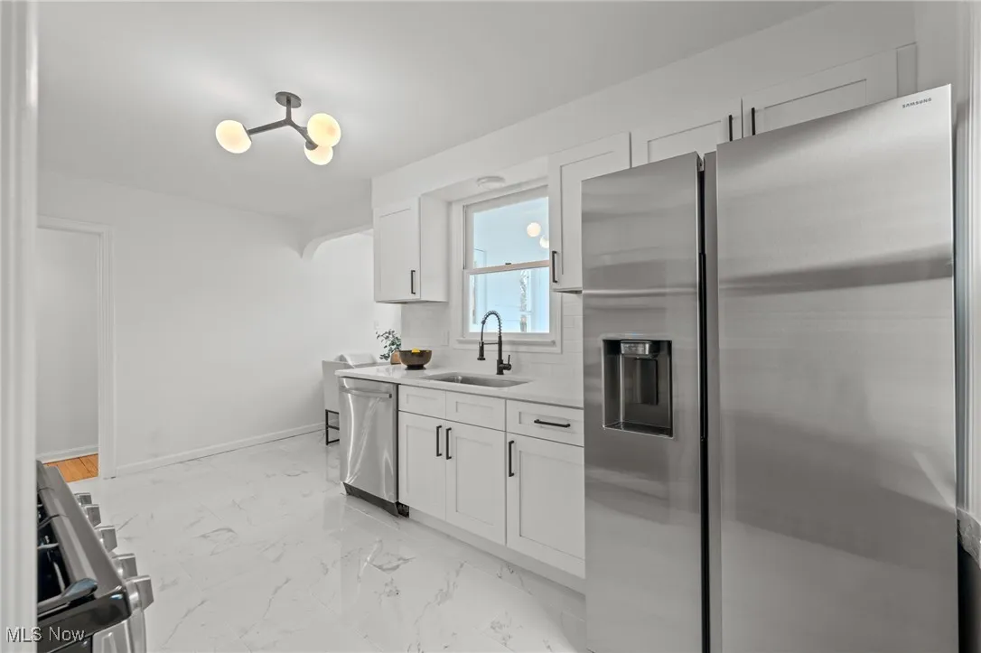 Kitchen with appliances with stainless steel finishes, white cabinetry, light marble finish flooring, tasteful backsplash, and light stone counters